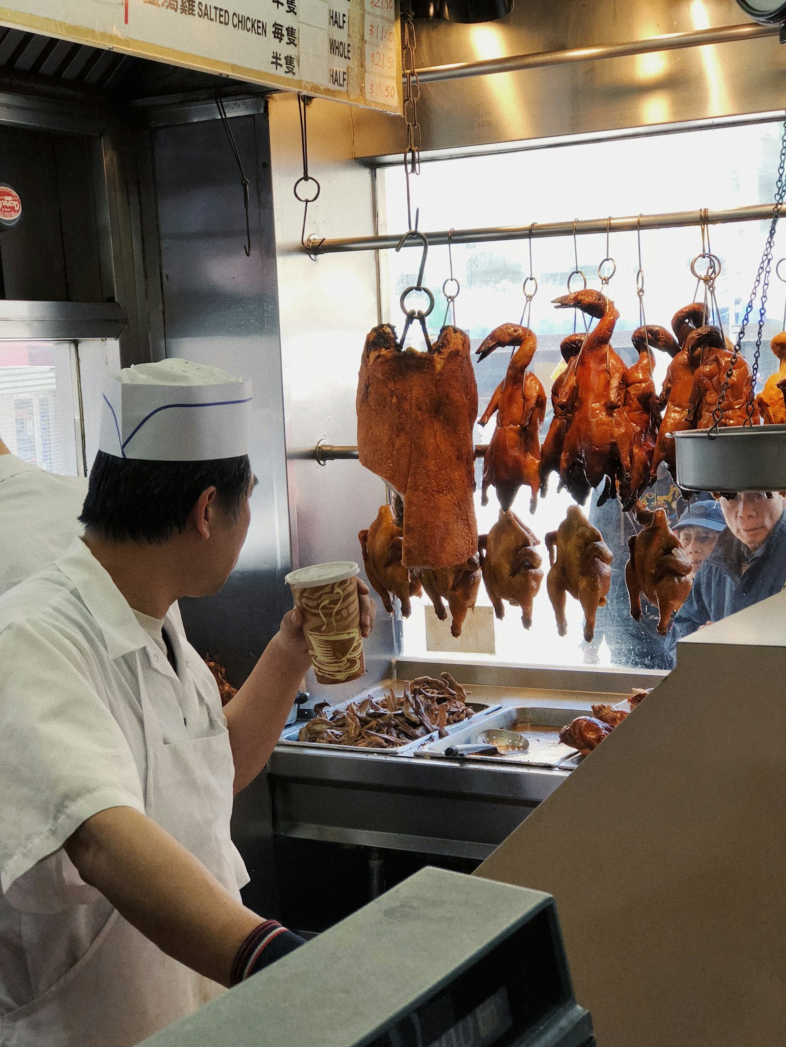 Chef in front of roast ducks hanging in a Chinese barbecue kitchen